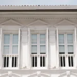 نمای کلاسیک ساختمان با ستون‌های عمودی و قاب‌بندی برجسته، شامل سه پنجره با قاب سفید و تزئینات مثلثی در بالای هرکدام؛ مناسب برای مقاله‌ای درباره طراحی و اجرای نمای کلاسیک از ایده تا اجرا.