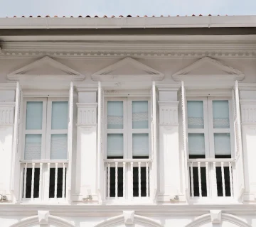 نمای کلاسیک ساختمان با ستونهای عمودی و قاببندی برجسته، شامل سه پنجره با قاب سفید و تزئینات مثلثی در بالای هرکدام؛ مناسب برای مقالهای درباره طراحی و اجرای نمای کلاسیک از ایده تا اجرا.