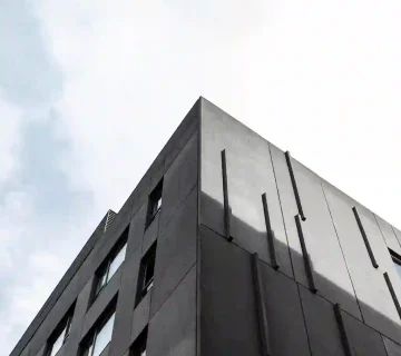 «نمای خارجی ساختمان مدرن با پنل‌های سیمانی تیره و خطوط عمودی برجسته، نمونه‌ای از اجرای طرح سنگ سیمانی با بافت یکدست و ظاهر مینیمال»