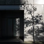 طراحی نمای مینیمال ساختمان با دیوار سنگی خاکستری و سایه درخت روی سطح آن، نشان‌دهنده سادگی و زیبایی در طراحی مینیمال معماری مدرن.